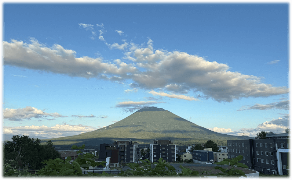 ニセコ比羅夫から眺める羊蹄山。青空の下に羊蹄山が美しく日に照らさられて輝いている。手前には建物がある。